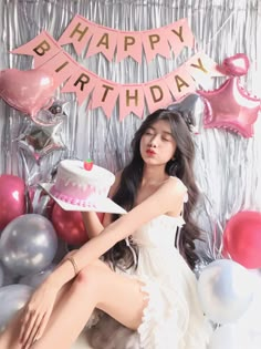 a woman sitting in front of a birthday cake with balloons and streamers around her