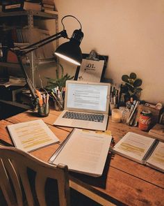 an open laptop computer sitting on top of a wooden desk next to two notebooks