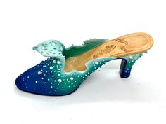 a pair of blue and green shoes with pearls on the heel, sitting on a white surface