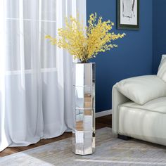 a vase with some yellow flowers in it next to a white couch and window sill