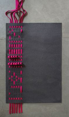 a piece of art made out of black paper with pink strips hanging from it's sides