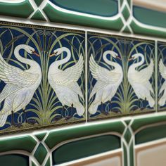 two white swans are depicted in this art deco tile design on the wall above a toilet