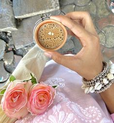 a person holding a cupcake in their hand next to some pink roses and flowers