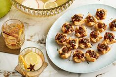 small appetizers are arranged on a plate next to a bowl of fruit and glasses