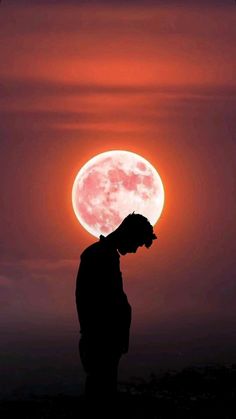 the silhouette of a man standing in front of a full moon at night with red clouds