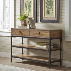 a console table with two drawers and books on it in front of some framed pictures