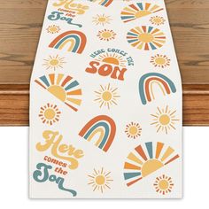 a white table runner with sun, rainbows and words on the side that says here comes the son