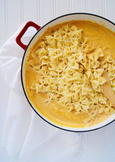 a pot filled with pasta and sauce on top of a white cloth next to a wooden spoon