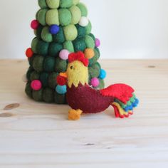 a small toy chicken standing next to a christmas tree with pom - poms