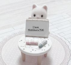 a small white cat sitting on top of a table with a note attached to it