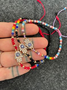 -----Price per Item----- This beautiful beaded bracelet have a unique small Hamsa charm with a small red evil eye in the center of the Hamsa. A unique bracelet that will keep you save and in style at the same time. You can choose between 5 different colors, you can see each style has a number for you to know which one you are choosing. These make the perfect couples and friendship gifts. A most have size adjustable everyday day bracelet. The Hamsa in these bracelets are 1.5cm- 0.60 inch long. ⚡️ Spiritual Adjustable Evil Eye Bracelet With Colorful Beads, Cheap Handmade Evil Eye Bracelet, Adjustable Spiritual Evil Eye Braided Bracelet, Spiritual Hand-strung Evil Eye Bracelet For Friendship, Hamsa Bracelet Evil Eye, Tibetan Ring, Bohemian Adjustable Hand-strung Evil Eye Bracelet, Hamsa Evil Eye, Evil Eye Hamsa