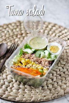 a plastic container filled with salad on top of a woven place mat next to a fork and knife