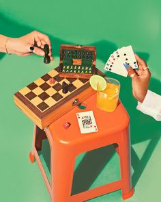 two people playing checkers on a small table with orange stools and green background