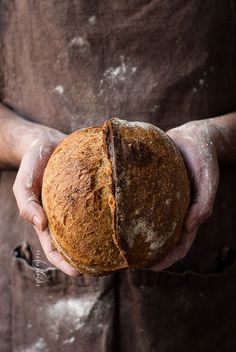 a person holding a loaf of bread in their hands with dirt all over the surface