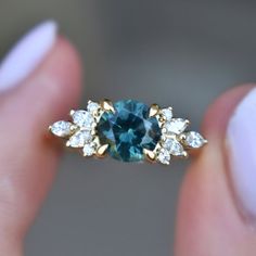 a woman's hand holding a ring with a blue stone surrounded by white diamonds