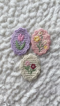 three crocheted flowers sitting on top of a white blanket next to each other