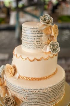 a three tiered wedding cake with roses on top and an old book page in the middle