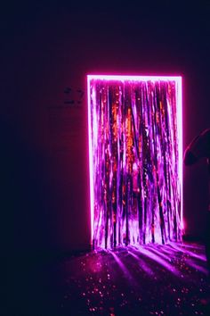 a person standing in front of a purple and pink wall with lights on the floor