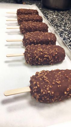 chocolate covered popsicles lined up on top of a baking sheet with wooden sticks sticking out of them