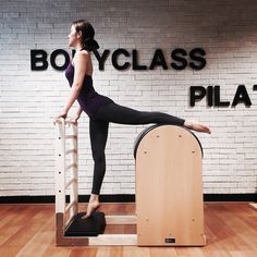 a woman standing on top of a chair in front of a sign that says body class pilat