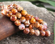 Capture the essence of earthy elegance with our cinnamon swirl agate rounds. Their warm tones pair with the subtle beauty of patterned agate perfectly. Ideal for creating anything from rustic bracelets to matching necklace sets. Sold as: 15" strand (approximately 48 beads per strand) Satisfy your desire for the whole rainbow with agate beads! When natural agate is dyed or heat-treated, the swirling or banding patterns in the stone are enhanced and vivid in coloration. The name Agate is associated with the Achates River of Sicily, now known as the Dirillo River. Agate was utilized by ancient Greeks and Romans for decorative carving and arts, and examples from that time are still extant. The colorful agate beads you see here have been dyed or heat-treated to achieve their bold coloring. Agat Rustic Bracelet, Earthy Elegance, Subtle Beauty, Cinnamon Swirl, Necklace Sets, Beads Online, Bead Store, Matching Necklaces, Agate Beads