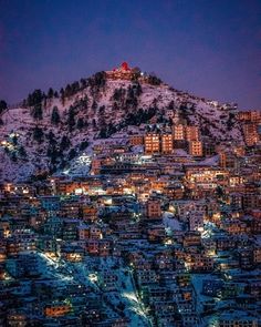 the city lights are lit up at night in the snow covered mountain side town below