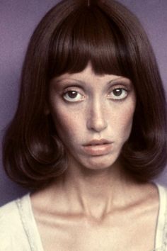 a woman with brown hair and blue eyes is posing for a photo in front of a purple background