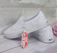 two pairs of white shoes with pearls on them and a pink flower in the background