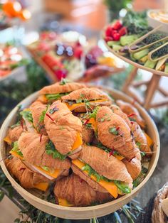 sandwiches and croissants are arranged in a bowl on a table with other food items