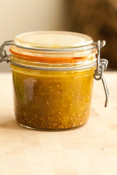 a glass jar filled with mustard sitting on top of a wooden table