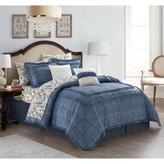 a bed with blue comforter and pillows in a room next to a lamp on a table