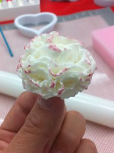 a hand holding a cupcake with white frosting and sprinkles on it