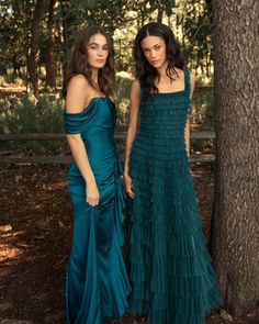 two women standing next to each other in front of a tree wearing dresses with ruffles