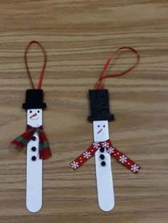 two snowmen made out of popsicle sticks sitting on top of a wooden table