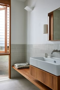 a bathroom sink sitting under a window next to a wooden shelf with a towel on it