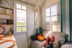 a person's feet resting on a couch in front of a window with a guitar