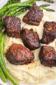 some meat and mashed potatoes on a white plate with asparagus in the foreground