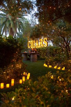 people are sitting at a table in the middle of a garden with lit candles around it