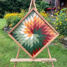 a wooden easel holding a colorful quilt on it's side in the grass