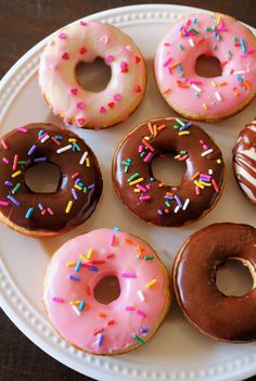 six donuts with chocolate frosting and sprinkles on a white plate