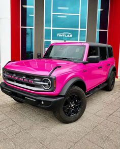 a bright pink truck is parked in front of a building with red and blue windows