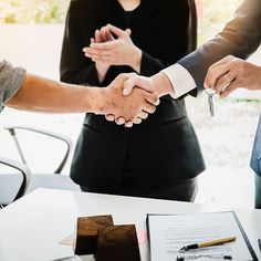 three people shaking hands over a table with papers and pens on it, while another person holds the other hand