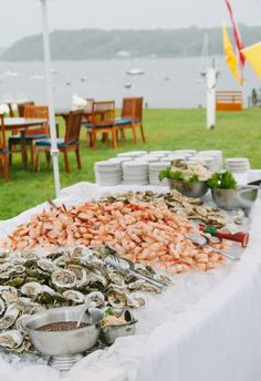 a table with food on it in the middle of a grassy area next to a body of water