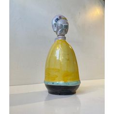 a yellow and black vase sitting on top of a white table next to a lamp