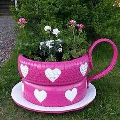 a pink watering can with hearts painted on it and flowers in the center, sitting outside