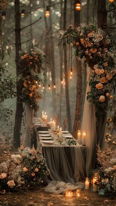 a long table with candles and flowers on it in the middle of a wooded area