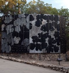 a large black and white painting on the side of a wooden fence in front of trees