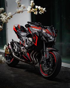 a red and black motorcycle parked in front of a building with white flowers on it