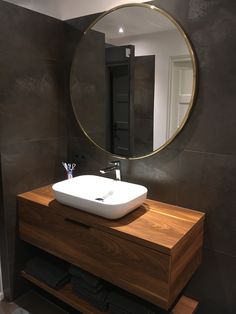 a bathroom sink sitting under a round mirror in front of a wall mounted faucet