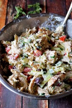 a bowl filled with chicken salad on top of a wooden table next to a spoon